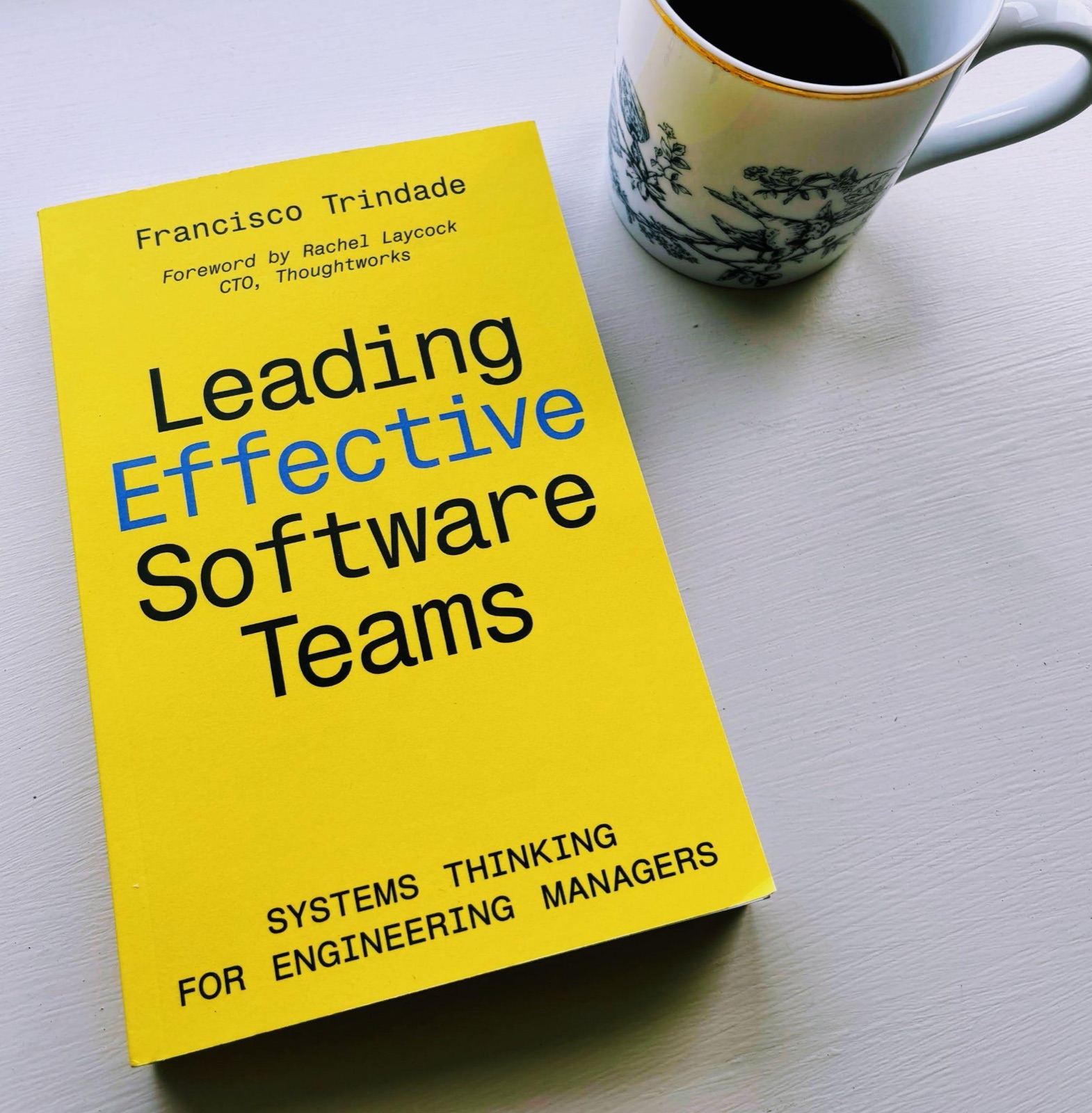 Leading Effective Software Teams, the printed book, next to a cup of coffee